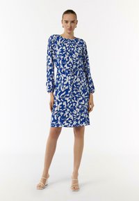 Blau-weiß gemustertes Kleid mit langen Ärmeln, Rundhalsausschnitt und Kordelzug in der Taille. Der Stoff scheint glatt zu sein und eignet sich sowohl für Freizeit- als auch für formelle Anlässe.