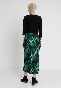 Top negro de manga larga combinado con una falda verde que presenta un patrón abstracto negro, hecha de tela suave, de longitud hasta los tobillos y con un diseño fluido.