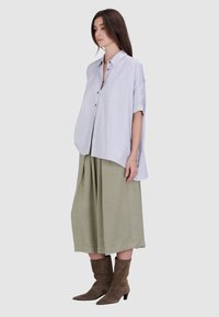 Lichtblauwe oversized shirt met korte mouwen, enkele borstzak, gecombineerd met een lange olijfgroene rok en bruin suède enkellaarsjes.