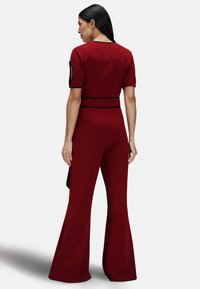 Tutina rossa aderente con maniche corte, pantaloni svasati, dettagli in nero e un design elegante. Tessuto morbido e materiale liscio.