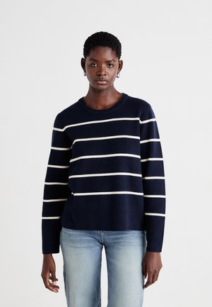 Granatowy sweter w paski z białymi poziomymi liniami, dzianinowa tekstura, okrągły dekolt i długie rękawy, w zestawieniu z jasnoniebieskimi dżinsami.