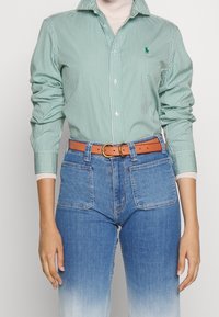 Zeleno-bíle pruhovaná košile s dlouhým rukávem a límečkem, spárovaná s modrými džínami a hnědým koženým páskem se zlatou sponou.