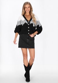 Svart och grå stickad cardigan med stora knappar och V-ringning, tillsammans med en svart denimkjol och svarta cowboystövlar.