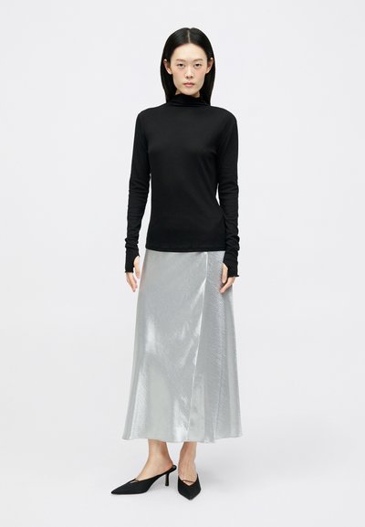 Črna dolga majica z dolgimi rokavi in sijoča srebrna midi krila. Krilo ima gladko teksturo in A-linijski kroj. Črne pete z ostrim nosom.