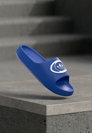 Sandalia tipo chancla azul hecha de material sintético liso, con diseño de punta abierta y un acento de logo blanco en la correa.