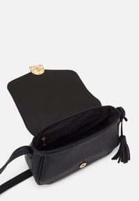 Czarna skórzana torebka na ramię z złotymi okuciami, ozdobą z frędzli oraz przestronnym wnętrzem wyposażonym w kieszeń na zamek i miękką podszewkę.