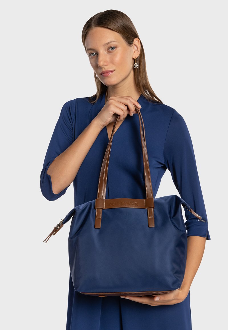 Borsa tote in nylon blu navy con dettagli in pelle marrone, due spallacci e chiusura superiore con zip. Presenta tasche laterali e finitura texturizzata.