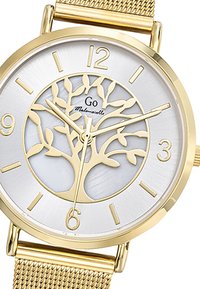 Montre pour femme en or avec un design d'arbre au centre, cadran argenté, marqueurs d'heure en or et bracelet en maille dorée. Élégante et détaillée.