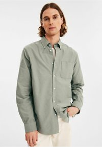 Lichtgroene blouse van zacht stof, met een borstzak, klassieke kraag en knopenmanchetten, gecombineerd met lichtgekleurde broek.