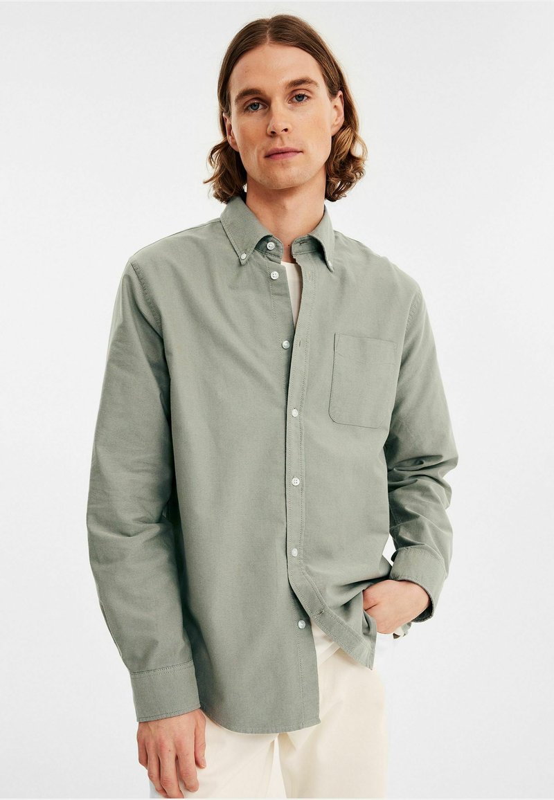 Lichtgroene blouse van zacht stof, met een borstzak, klassieke kraag en knopenmanchetten, gecombineerd met lichtgekleurde broek.