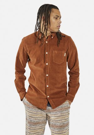Bruine corduroy shirt met een button-down kraag, een enkele borstzak en witte knopen, gecombineerd met gemusterde, multikleurige broeken.