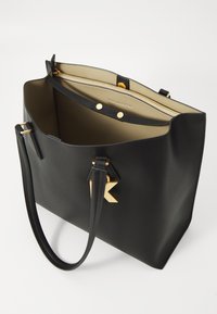 Geantă de tote din piele neagră cu accesorii din aur, dotată cu o închidere prin fermoar superior și buzunare interioare. Textură netedă, formă structurată, branding minim.