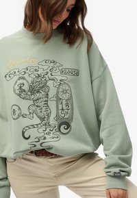 Mintgroene sweatshirt met geborduurde tijgerprint en merknamen. Beschikt over geribbelde manchetten en een ronde halslijn. Ontspannen pasvorm.