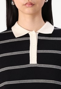 Black and ivory striped polo shirt with a collared neckline, three button placket, and soft knit texture.