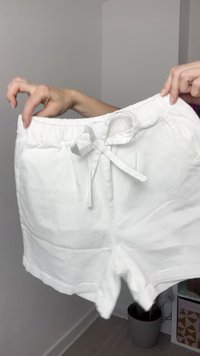 Pantaloni corti bianchi in cotone con vita regolabile, caratterizzati da un orlo che termina sopra il ginocchio e una texture liscia e leggera.