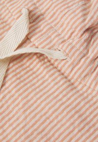 Cotton fabric with alternating orange and white stripes, featuring a beige textile loop and visible stitching details.