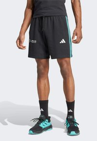 Pantalones cortos deportivos negros hechos de tela transpirable, con franjas laterales en color teal, cintura con cordón y un logo blanco en el lado izquierdo.