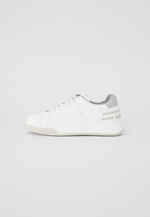 Valkoinen matalakärkinen tennari, jossa nauhat edessä, rei'itetyt sivuosiot ja harmaat yksityiskohdat kannassa ja vuorauksessa.