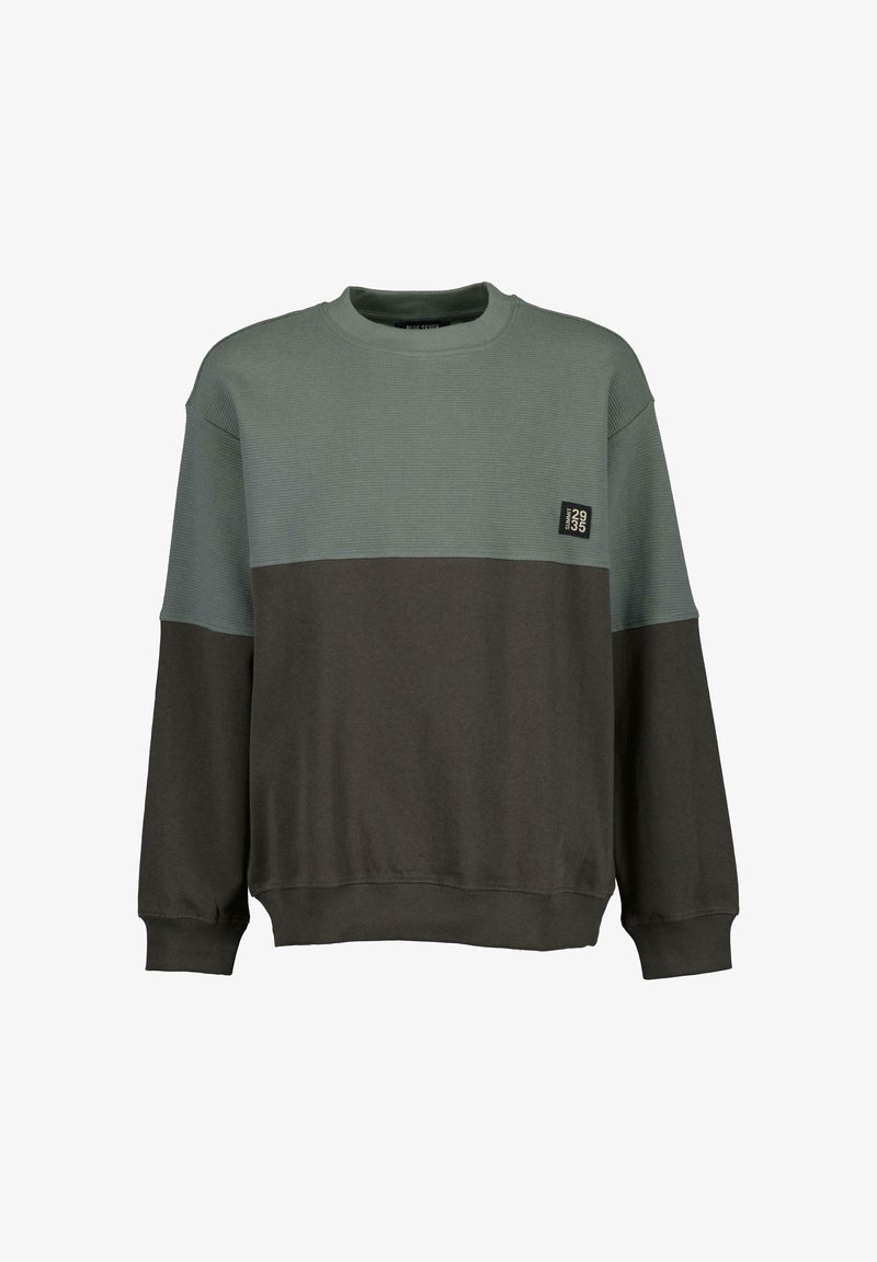 Sweat-shirt col rond avec moitié supérieure à texture côtelée en vert doux et moitié inférieure lisse en brun foncé, avec une petite écusson noire sur la poitrine.