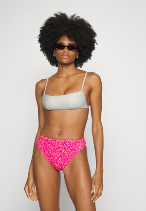 Top de bikini texturizado cinza com alças finas e parte de baixo de bikini com padrão de leopardo rosa. Modelo usa óculos escuros escuros; tom de pele suave visível.