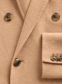 Blazer en laine beige avec un design croisé, de gros boutons circulaires et une poche passepoilée ornée de trois boutons assortis.