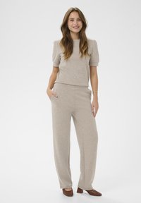 Bežový pletený top s krátkymi puff rukávmi v kombinácii so zodpovedajúcimi širokými nohavicami. Pohodlný materiál, minimalistický dizajn a bočné vrecká na nohaviciach.
