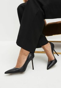 Dei tacchi alti neri in pelle con punta affilata, caratterizzati da una texture liscia e elegante e un sottile tacco a spillo.