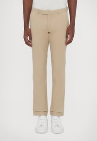 Beige chinos med slim fit, med platt front, bälteshällor och fint fållade muddar, i kombination med vita sneakers.