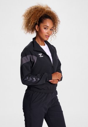 Zwarte sportjacket met grijze accenten, rits aan de voorkant en elastische boorden. Beschikt over een logo op de borst en een chevronpatroon op de mouwen.