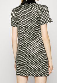 Svart och vit kort klänning med hounds-tooth mönster, puffärmar och svart sammetshals. Slät textur med en lätt lyster.