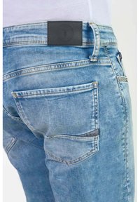 Lichtblauwe denim jeans met een versleten textuur, voorzien van een zwart leren label op de tailleband en twee achterzakken.