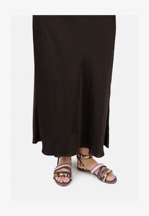 Barna, lágy esésű ruha, enyhe fény csillogással és oldalsó hasítékokkal. A lábbeli állatmintás, széles pántokkal és lapos talppal rendelkezik, barna és rózsaszín árnyalatokban.