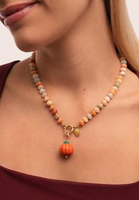 Collar de cuentas con piedras en tonos pastel, un charm de calabaza naranja y herrajes dorados con un pequeño colgante decorativo.