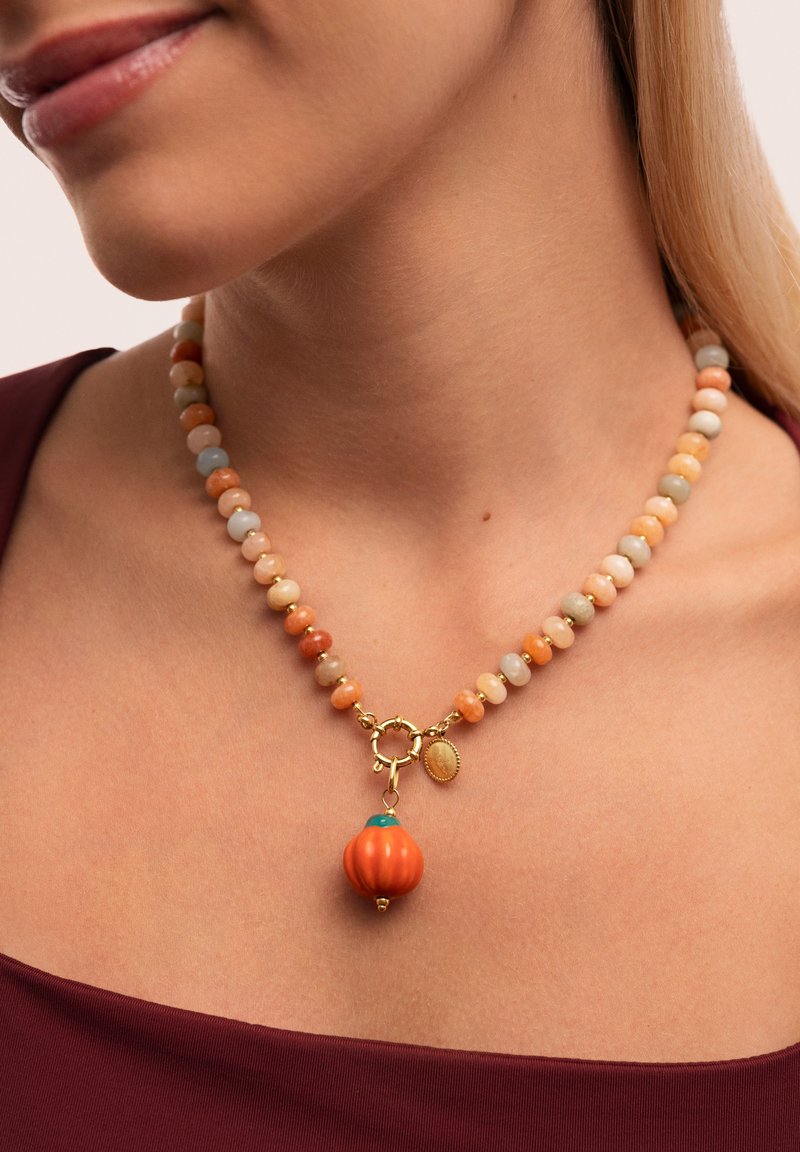 Collar de cuentas con piedras en tonos pastel, un charm de calabaza naranja y herrajes dorados con un pequeño colgante decorativo.