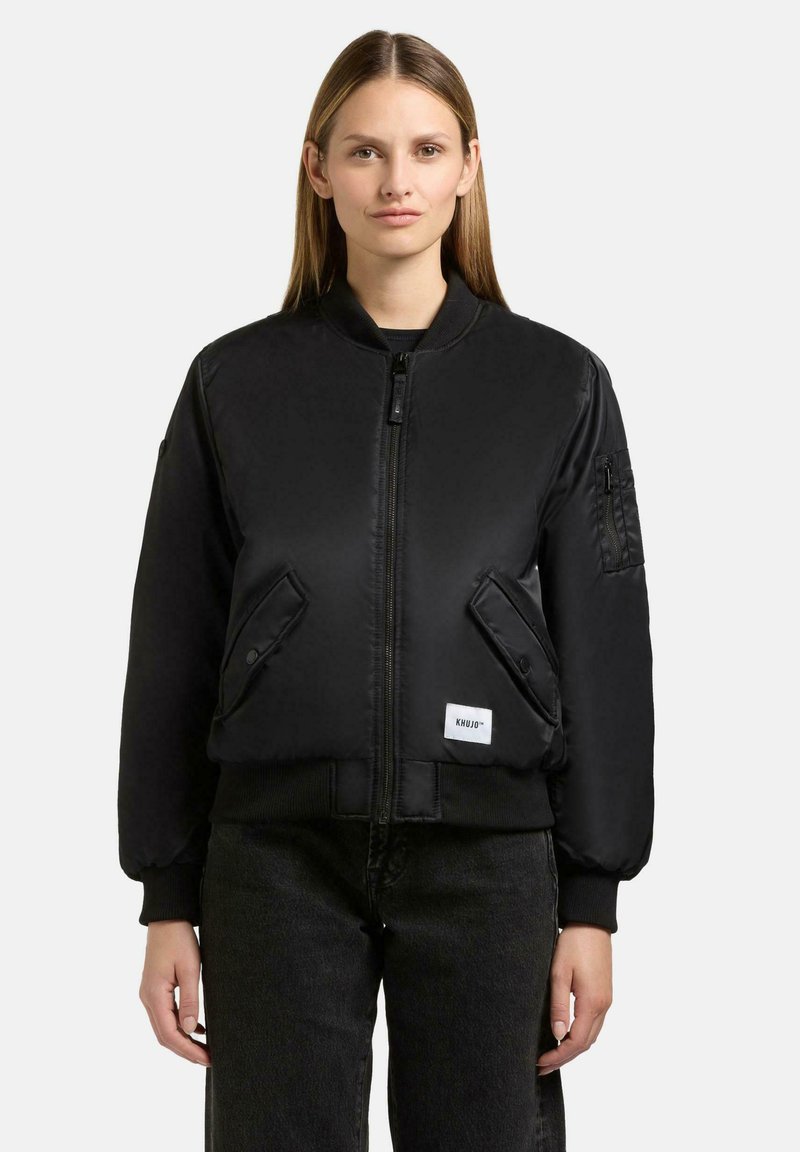 Schwarze Bomberjacke mit Reißverschluss vorne, gerippten Bündchen und zwei schrägen Taschen. Mit einem Logo-Patch auf der unteren linken Seite und einer Taschen an den Ärmeln.