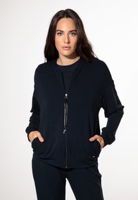 Marinefarbener Reißverschluss-Pullover mit lockerer Passform, ausgestattet mit zwei Fronttaschen und einer Kordelzugverschlus, aus weichem, dehnbarem Stoff hergestellt.