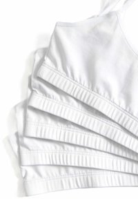 Fem enheter av vita bomullsbraletter med justerbara band, som har en ribbad kant och sömlös design för komfort.