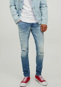 Ljusblå slitna jeans med revor och blekningar, ihopparat med röda sneakers. Tyget är denim och har en slim fit-design.