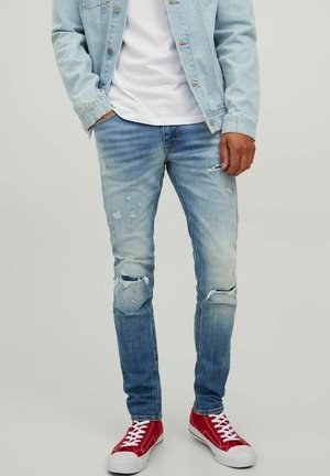 Vaqueros desgastados de color azul claro con desgarros y decoloración, combinados con zapatillas rojas. La tela es de mezclilla y tiene un diseño de corte ajustado.