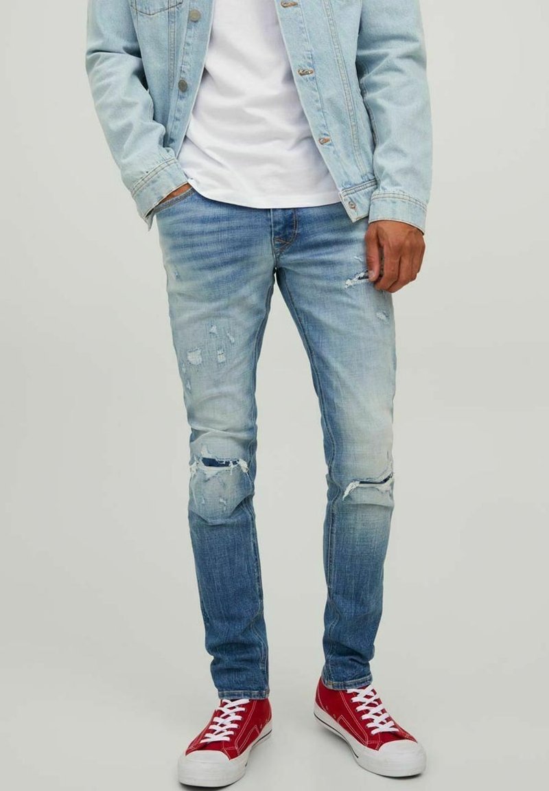 Ljusblå slitna jeans med revor och blekningar, ihopparat med röda sneakers. Tyget är denim och har en slim fit-design.