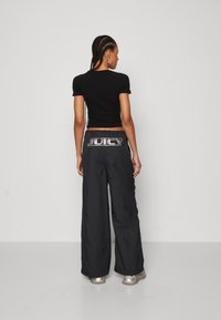 Black cropped t-shirt with short sleeves paired with black wide-leg pants featuring a silver "JUICY" logo on the back. Smooth texture.