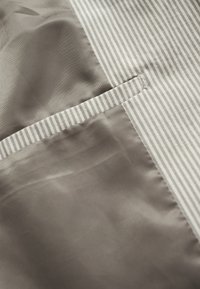 Grijze stof met een gladde textuur, met aan de ene kant een gestreept ontwerp en aan de andere kant een klein, gestikt zakje.