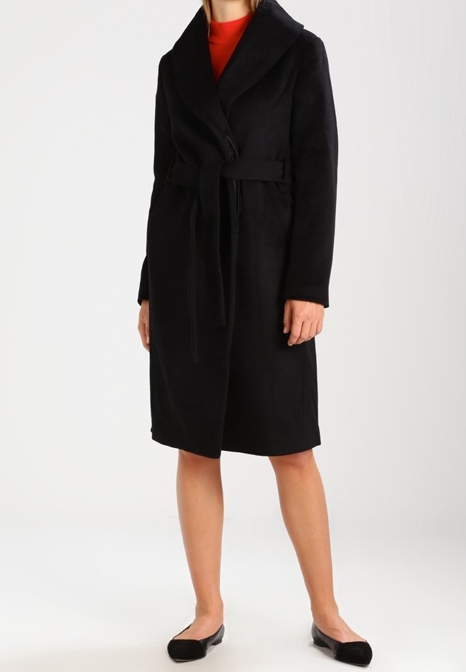 Cappotto nero con cintura, dotato di un ampio colletto, realizzato in materiale morbido. Presenta maniche lunghe e un design di lunghezza media. Indossato sopra una maglia rossa.