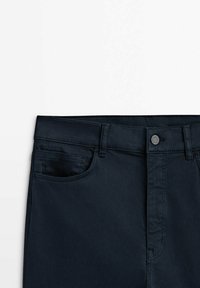 Ceinture de pantalon bleu marine foncé avec passants de ceinture, bouton devant, braguette à glissière et poche avant visible sur fond blanc.