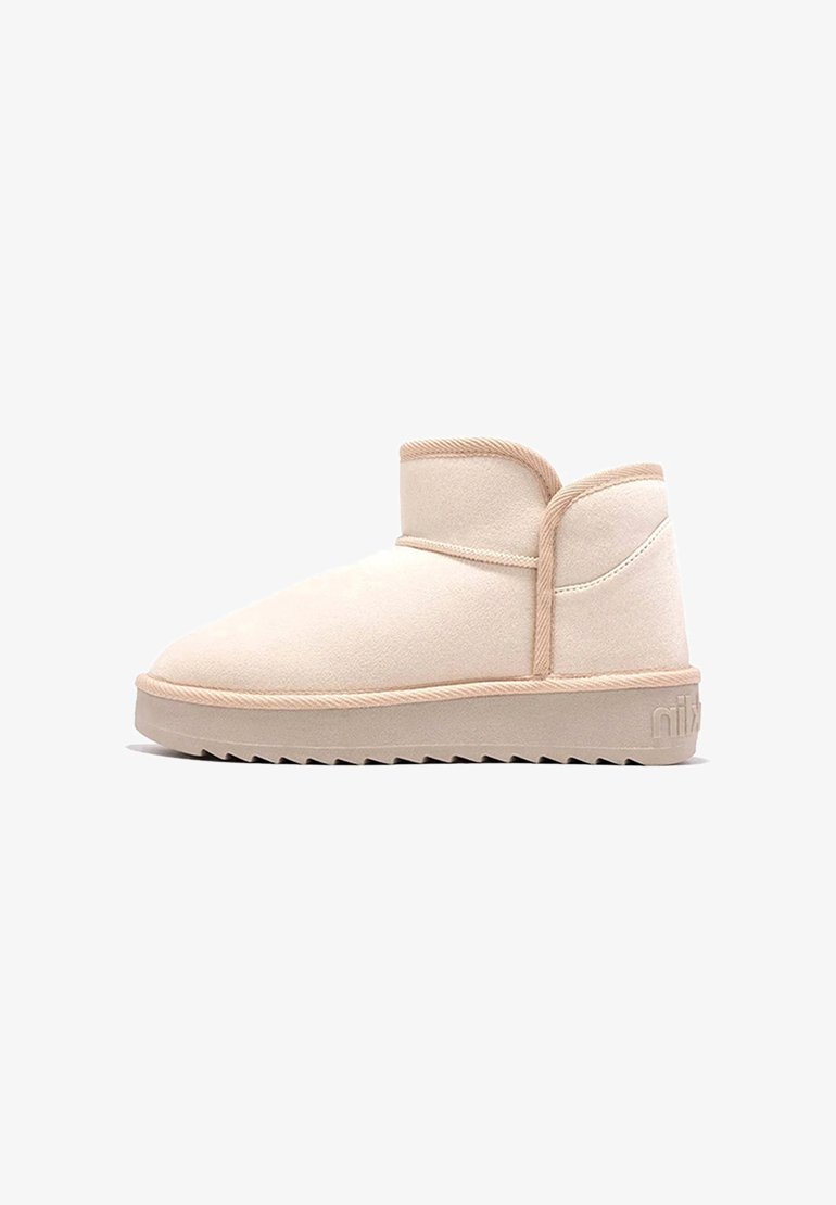 Botas de tobillo beige hechas de suave ante, con puntera redondeada, un ajuste ceñido alrededor del tobillo y suela de goma texturizada con un patrón de zigzag.