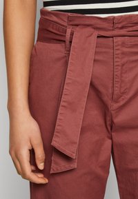 Pantalons taille haute ceinturés dans une couleur rose poussiéreux. Fabriqués en tissu lisse, avec une poche latérale et une ceinture en tissu texturé.