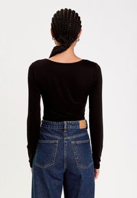 Chemise noire à manches longues associée à un jean en denim bleu taille haute. Le jean présente une étiquette en cuir beige à l'arrière et des coutures classiques.