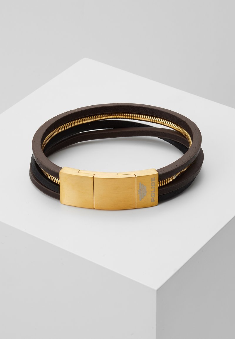 Bracelet en cuir marron avec fermoir en métal doré et détail en spirale, placé sur une surface géométrique blanche.