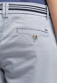 Jasnoniebieskie chinosy o gładkiej fakturze. Posiadają płaską tylnią kieszeń z zapięciem na guzik oraz paskiem w paski.