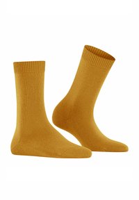 Un paio di calzini a coste giallo senape su sfondo bianco, uno disteso e l'altro leggermente inclinato in posizione verticale.